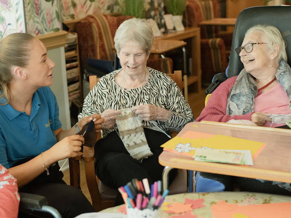 Care worker helping two older women with knitting